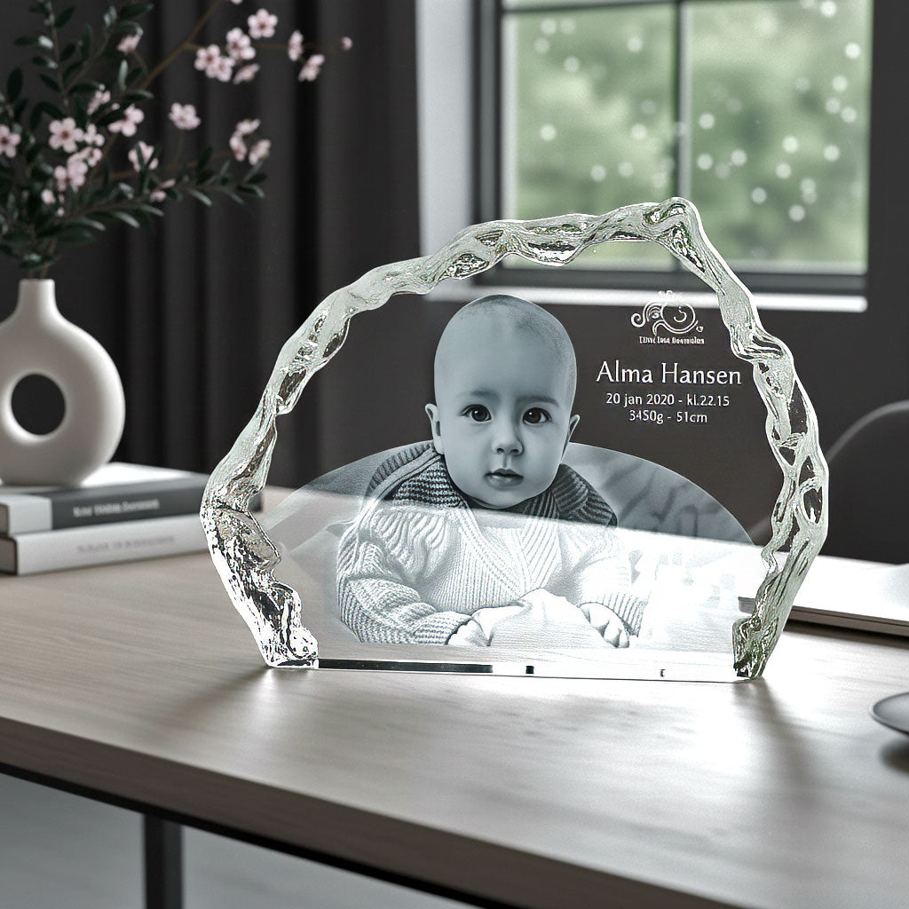 Iceberg-shaped glass block with engraved baby on a desk by the window