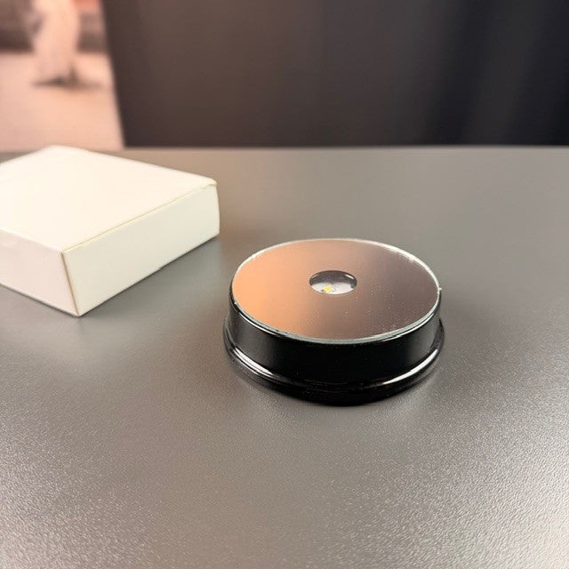 Black round battery light base next to the box