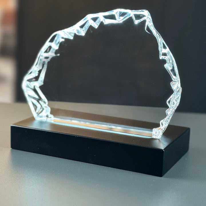 Iceberg-shaped glass block from the front on a lit matte black luxury light base 9x16 cm