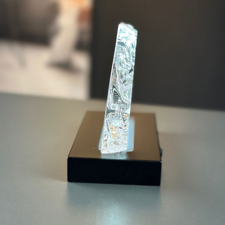 Iceberg-shaped glass block seen from the side on a matte black luxury light base