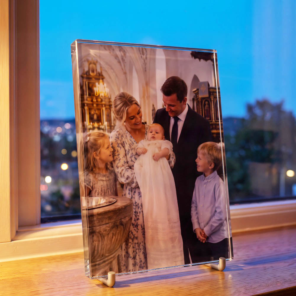 Print glass with colour print of a family photo from a christening, seen from the side on a windowsill