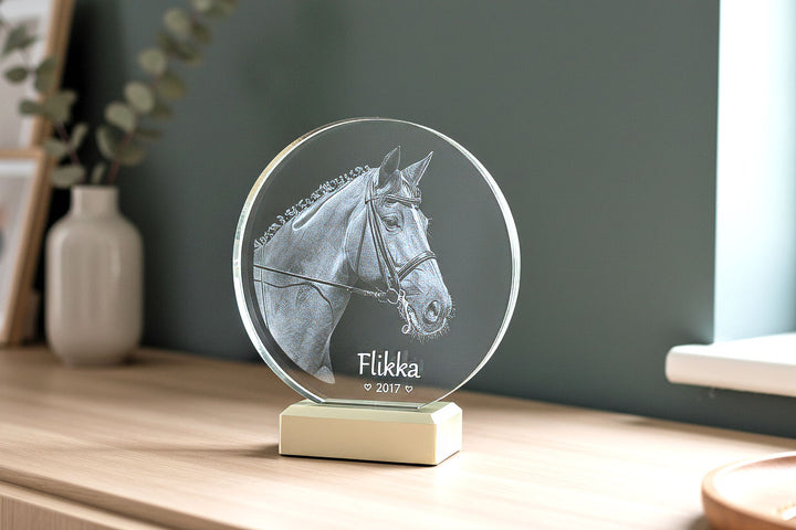 Round glass block with engraved horse head on a light-coloured light base in a living room