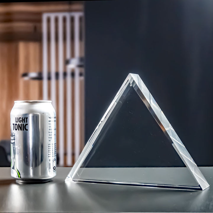Triangular crystal glass award next to a can for size